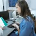 Nurse in scrubs typing on a keyboard at a medical workstation.