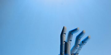 Robotic hand with articulated fingers reaching towards the sky on a blue background.