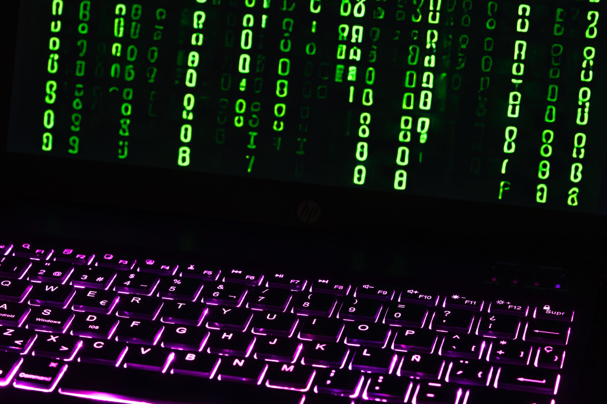 Illuminated laptop keyboard with Matrix-style green code cascading down screen.