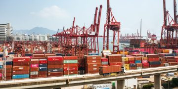 A bustling scene of cargo containers and cranes at a Hong Kong port, showcasing global trade.