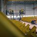A worker welding metal in an industrial warehouse with heavy machinery.