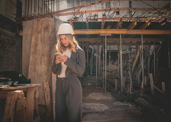 Young female engineer with hard hat checking phone at construction site.
