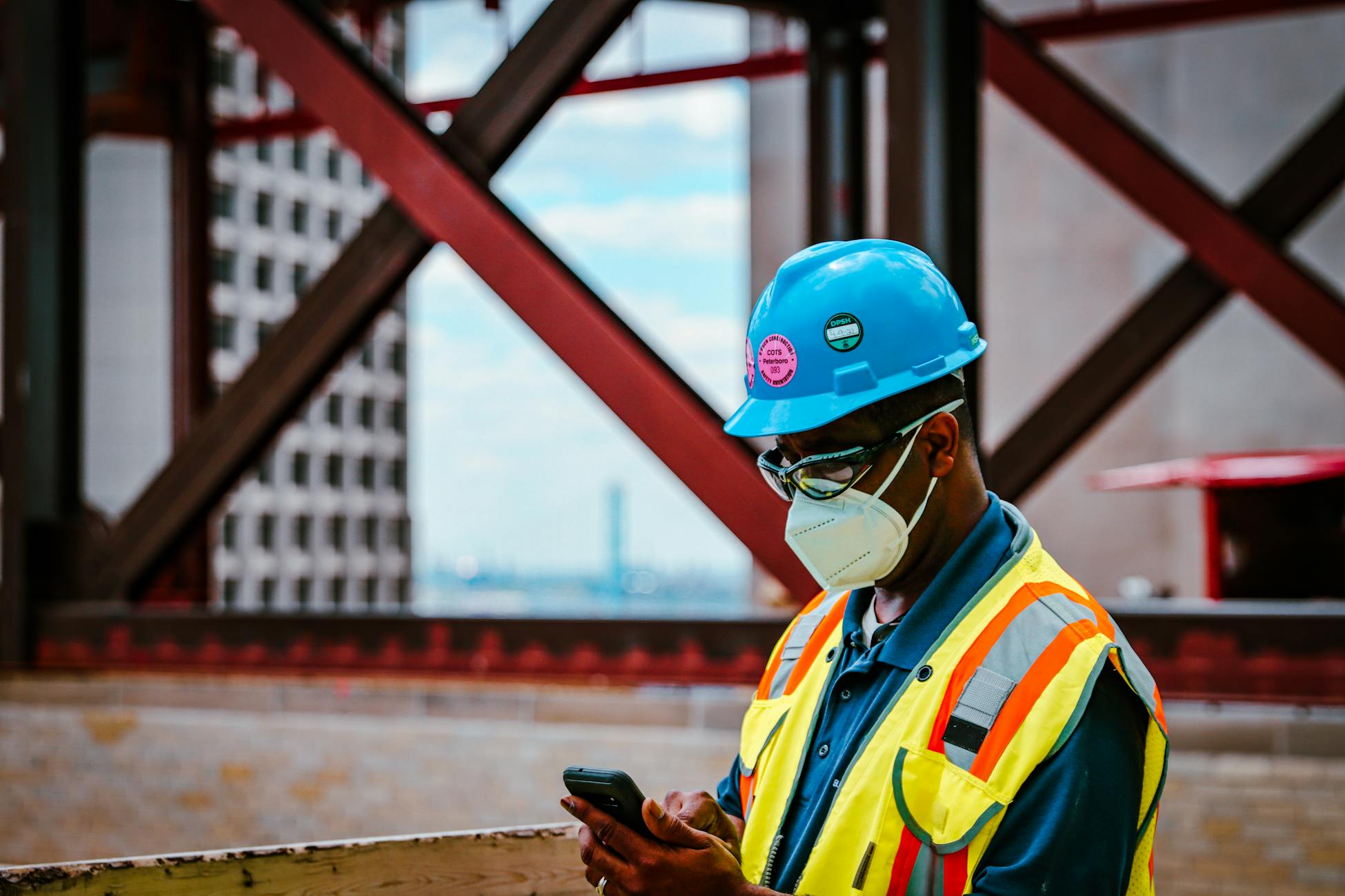 Construction worker in safety gear checking smartphone on a Detroit site.