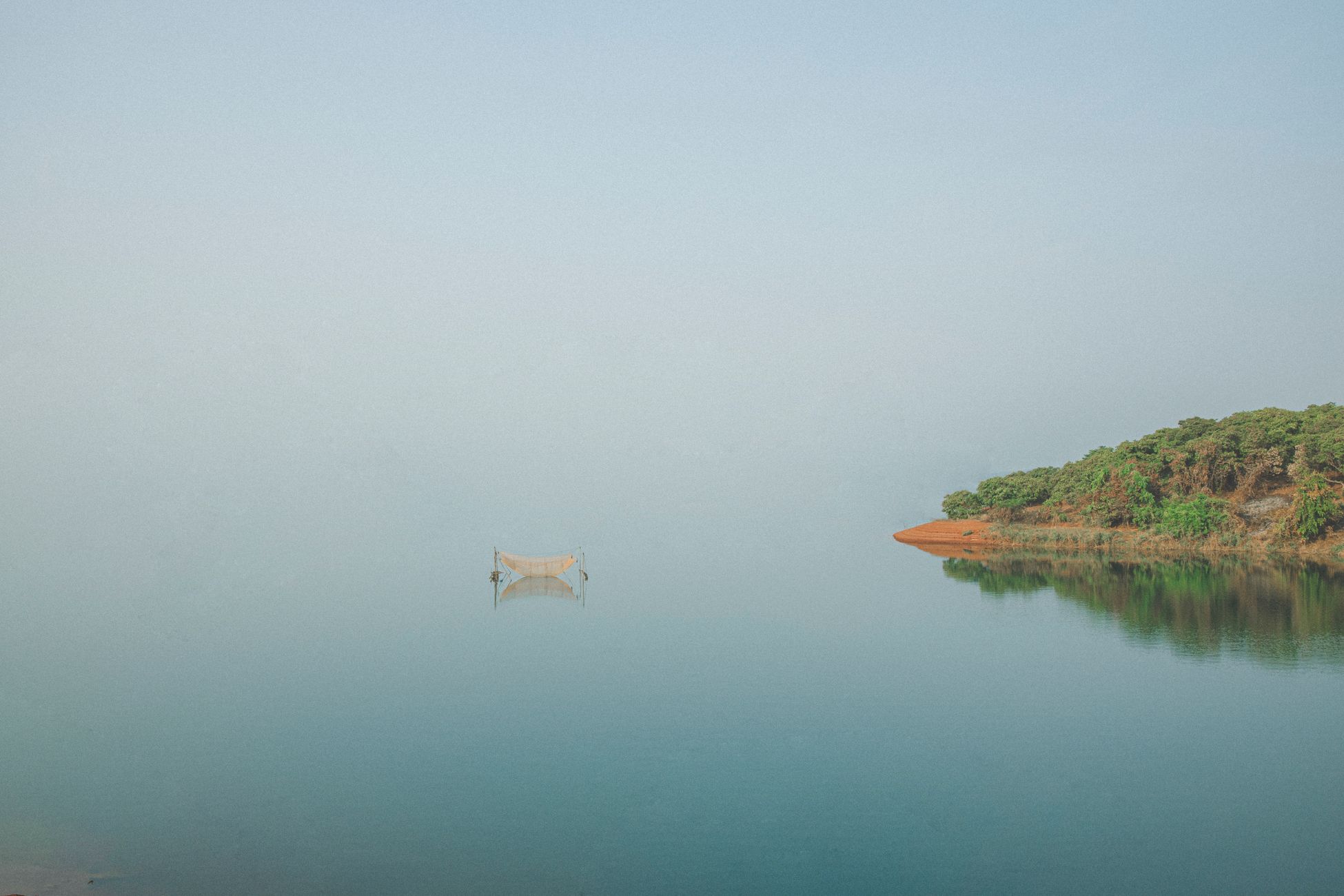Calm and soothing scene of a wooden boat on glassy water near lush green island.