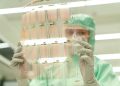 Scientist in protective gear holding a transparent test sheet in a laboratory.