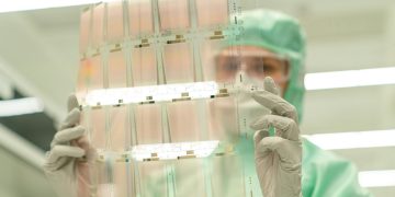 Scientist in protective gear holding a transparent test sheet in a laboratory.