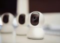 Close-up of three smart home security cameras placed on a white desk indoors.