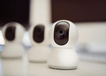 Close-up of three smart home security cameras placed on a white desk indoors.