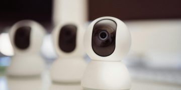 Close-up of three smart home security cameras placed on a white desk indoors.