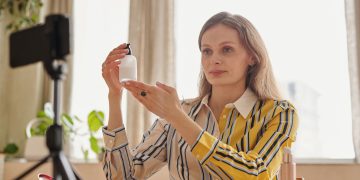 Woman demonstrates skincare product during a vlog in a cozy indoor setting.