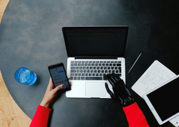 A person using a laptop, smartphone, and tablet with a prosthetic hand, emphasizing digital connectivity.