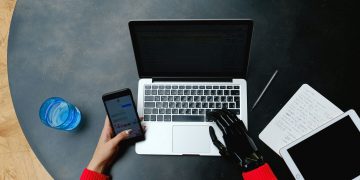 A person using a laptop, smartphone, and tablet with a prosthetic hand, emphasizing digital connectivity.
