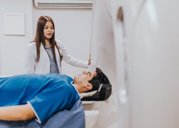 A doctor stands beside a patient in an MRI room, ensuring a smooth examination process.