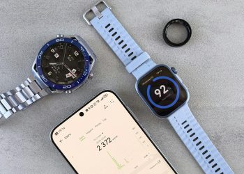 Smartwatch, ring tracker, and smartphone displaying fitness data on a gray surface.