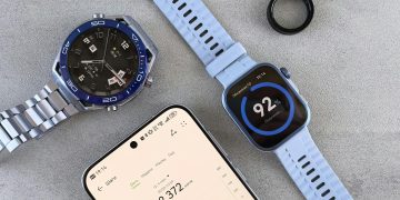 Smartwatch, ring tracker, and smartphone displaying fitness data on a gray surface.