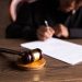 Judge signing documents at desk with focus on gavel, representing law and justice.