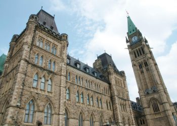 A view of the historical Parliament Hill building in Ottawa against a clear sky.