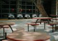 Futuristic delivery robots lined up near outdoor cafeteria tables, showcasing modern technology.