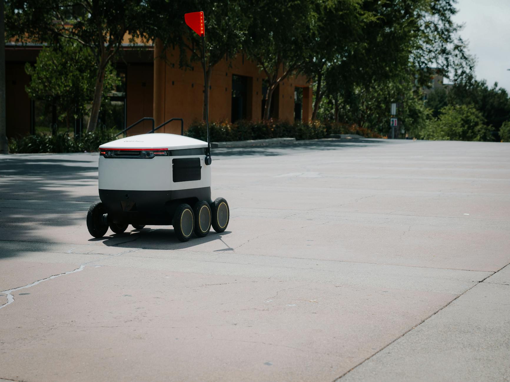 A sleek autonomous food delivery robot navigates a sunny urban landscape, showcasing modern innovation.