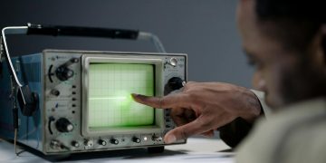 Close-up of a person pointing at a vintage oscilloscope screen in a tech setting.