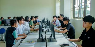 Diverse group of students studying in a computer-equipped classroom setting.