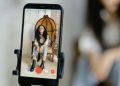 A woman sits in a chair recording a video on her smartphone, showcasing modern vlogging techniques.