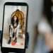 A woman sits in a chair recording a video on her smartphone, showcasing modern vlogging techniques.