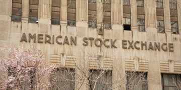 Facade of the American Stock Exchange Building in New York City during spring with blooming trees.