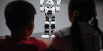 Two children observe a humanoid robot on a table, exploring technology and innovation.