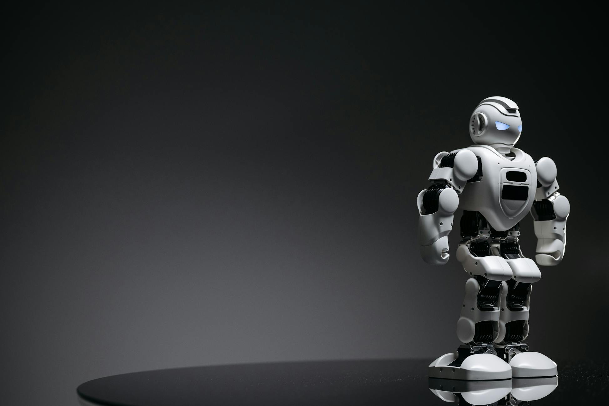 Compact humanoid robot toy standing on a reflective surface, exuding a futuristic vibe.