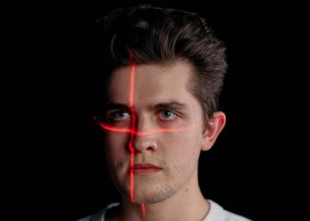Conceptual portrait with laser scanning for facial recognition on plain black background.