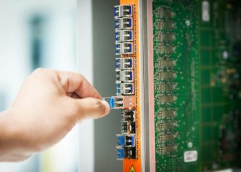 An individual connecting a cable into a network server port indoors, focusing on technology setup.