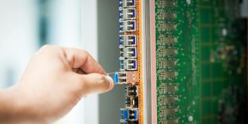 An individual connecting a cable into a network server port indoors, focusing on technology setup.