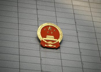 Close-up of the Chinese national emblem on a large concrete building facade, symbolizing government presence.