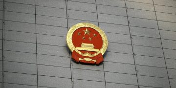Close-up of the Chinese national emblem on a large concrete building facade, symbolizing government presence.