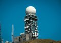 Imposing satellite tower with numerous dishes against a vibrant blue sky.