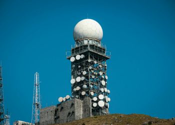 Imposing satellite tower with numerous dishes against a vibrant blue sky.