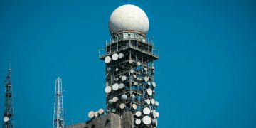 Imposing satellite tower with numerous dishes against a vibrant blue sky.