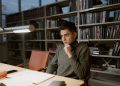 A man in a turtleneck sweater concentrates on studying in a library setting.