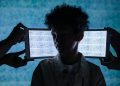 A teenager stands with eyes closed between two tablets showing digital noise, symbolizing information overload.