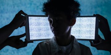 A teenager stands with eyes closed between two tablets showing digital noise, symbolizing information overload.