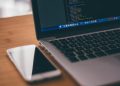 Coding setup with laptop displaying code and smartphone on a wooden table, ideal for tech themes.