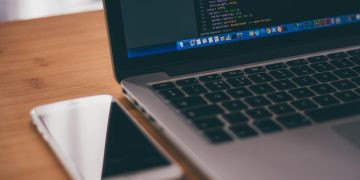 Coding setup with laptop displaying code and smartphone on a wooden table, ideal for tech themes.