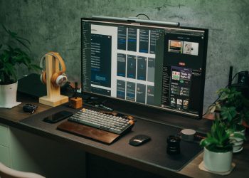A sleek home office setup featuring a large monitor, keyboard, plants, and headphones on a desk.