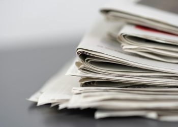 Close-up of stacked newspapers on a table, representing media and journalism.