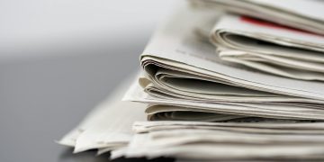 Close-up of stacked newspapers on a table, representing media and journalism.
