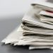 Close-up of stacked newspapers on a table, representing media and journalism.