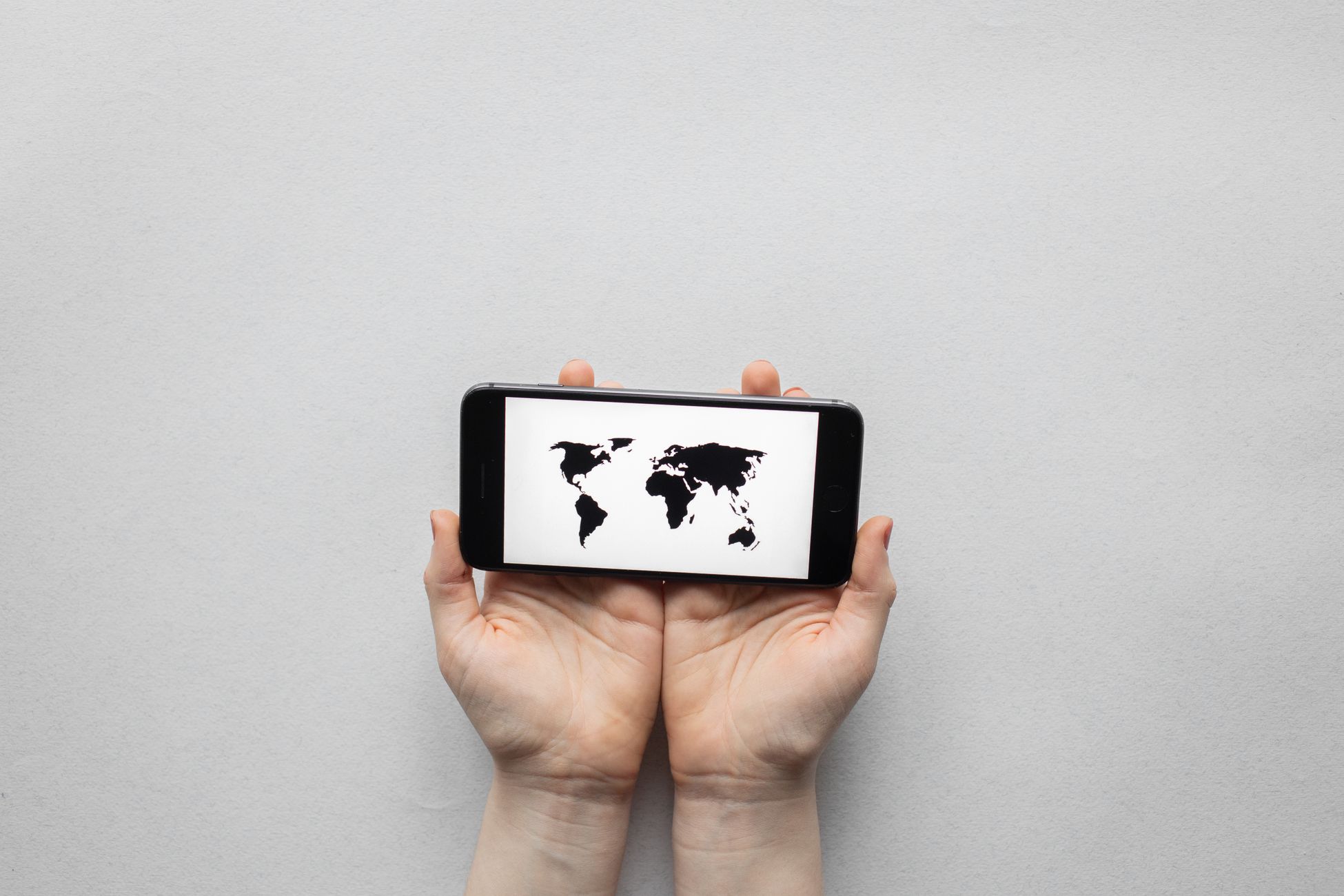 Hands holding a smartphone displaying a world map on a white background.