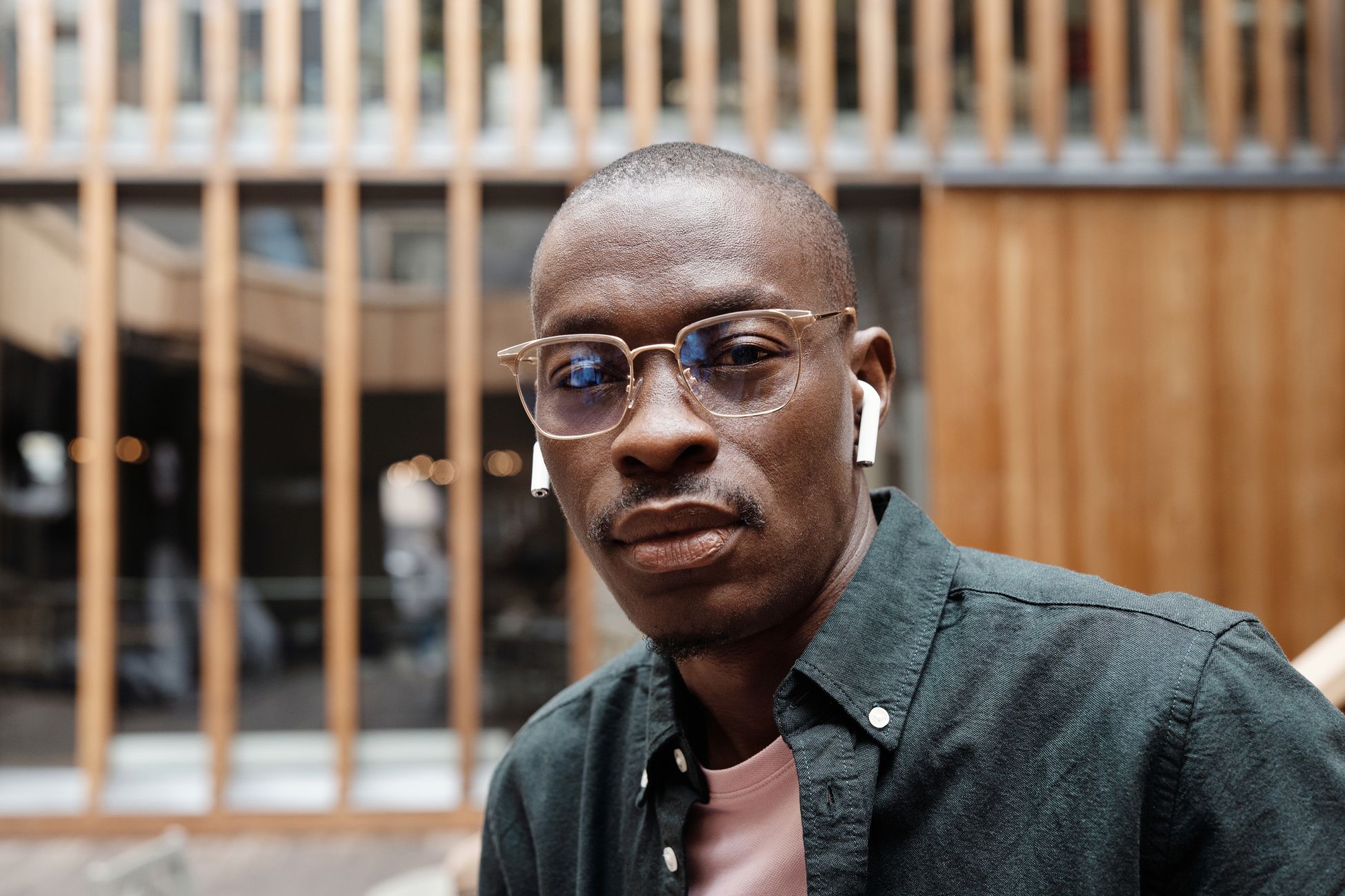 Bald African American man wearing glasses and earbuds, with a confident look, outdoors.