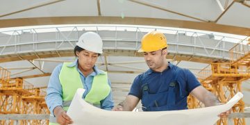Male and female engineers discussing blueprints at a construction site, promoting teamwork and planning.